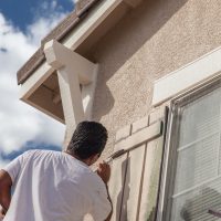 Un homme en train de peindre au niveau d'un volet sur le mur d'une maison