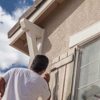 Un homme en train de peindre au niveau d'un volet sur le mur d'une maison