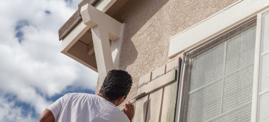 Un homme en train de peindre au niveau d'un volet sur le mur d'une maison