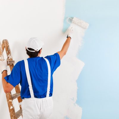 Un homme en tenue de travail, en train de peindre un mur en blanc